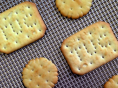 Three round biscuits and two rectangular biscuits on the flat rolled oven mesh belts.